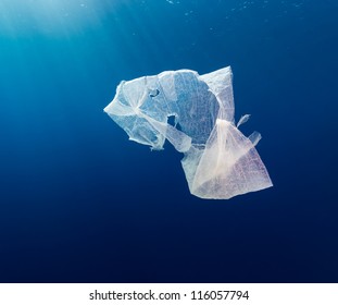 A waste plastic bag floating in deep water in open ocean with sun rays behind