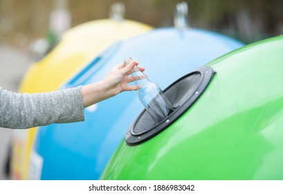 Waste Sorting And Recycling Concept. Unrecognizable Female Throwing Empty Glass Bottle Into Green Recycle Bin Garbage Container Outdoors, Caring About Environment, Cropped Image With Selective Focus