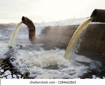 Wastewater From Two Large Rusty Pipes Merge Into The River In Clouds Of Steam