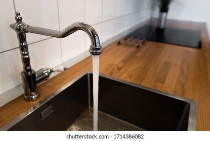 Wasting Water By Leaving A Chrome Faucet Tap Running. Water Flowing Out Of A Kitchen Stainless Steel Tap Into The Sink. Water Misuse In Domestic Duties And Activities. Overusing Household Water.