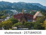 Wat Chalong temple in Phuket, Thailand, features a golden spire, red roofed structures, ornate carvings, lush greenery, and rolling hills in the background.