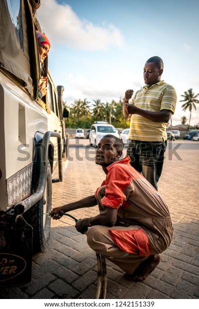 Watamu, Kenya - August\
2018: African man mechanic checking wheel\'s pressure on an off-road\
vehicle defender.