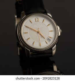 A watch with a leather strap on a dark background.                              