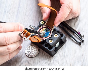 watch repairer workshop - watchmaker installs battery in quartz wristwatch with plastic tweezers on wooden table