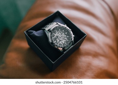 A watch is sitting in a box on a brown surface. The watch is silver and has a black face - Powered by Shutterstock