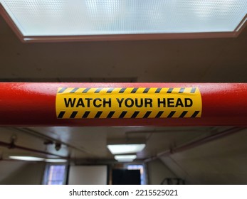 A Watch Your Head Sign Attached To A Large Red Pipe.