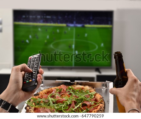 Watching the football game eating pizza,drinking beer holding television control.