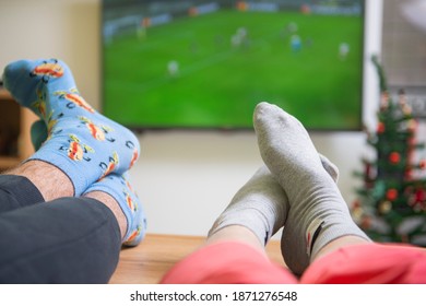 Watching A Football Game. View Of A Man And Woman Legs And Feet Relaxing  In Front Of The TV 