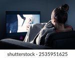 Watching horror and scary film on tv. Woman and thriller movie on television. Person in fear on home sofa couch under blanket at night in dark. Streaming true crime series or halloween show.