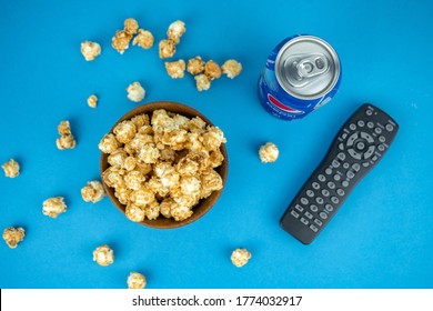 watching movie at home concept, cold refreshing blue pepsi can, wooden bowl of fresh caramel popcorn, remote tv control, top view. Kiev, Ukraine - July 2020