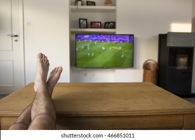 Watching a soccer match on TV with the feet on the table.