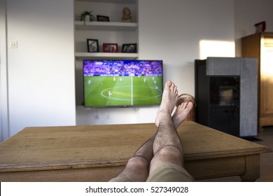 Watching A Soccer Match On TV With The Feet On The Table.