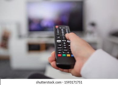 Watching TV and using remote controller. Hand with remote controller changing channels or opening apps on smart tv