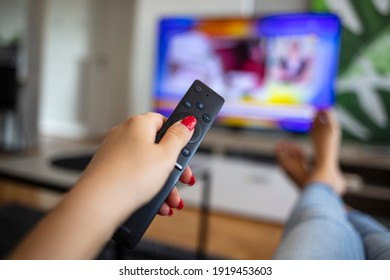 Watching TV and using remote controller. Hand with remote controller changing channels or opening apps on smart tv. Hand holding remote control with blurred TV set in the background