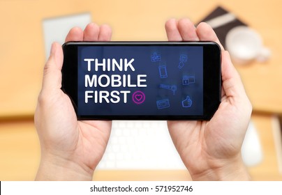 Watching Two Hand Holding Mobile Phone With Think Mobile First Word And Feature Icon With Blur Desk Office Background,Digital Marketing.