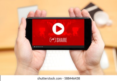 Watching Two Hand Holding Mobile Phone With Play And Share Video Icon On Screen And Blur Desk Office Background,Digital Content Concept