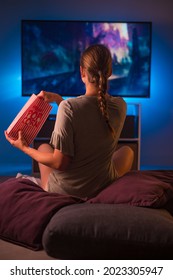 Watching your favorite movies and programs on TV. A young blonde woman sits in front of the TV with a packet of popcorn. Blue neon light. Relax. Hobby. Rest. Favorite TV shows. - Shutterstock ID 2023305947