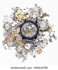 watchmaker workshop - top view of open mechanical watch on heap of old clock spare parts on white background