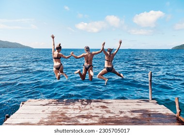 Water, back of people jumping off a pier holding hands and into the ocean together in blue sky. Summer vacation or holiday break, freedom or travel and young group of friends diving into the lake