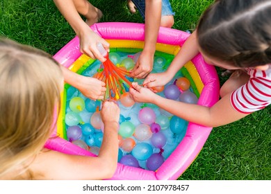 Water balloon games for kids. Close up of girls filling up water balloons at sunny day. Summer fun outdoor activities for children concept