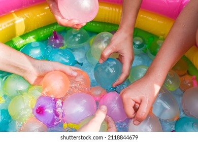Water balloon games for kids. Close up of girls filling up water balloons at sunny day. Summer fun outdoor activities for children concept