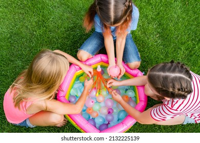 Water Balloon Games For Kids. Close Up Of Girls Filling Up Water Balloons At Sunny Day. Summer Fun Outdoor Activities For Children Concept