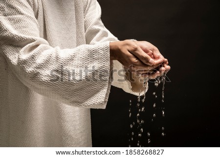 Water for Baptism pouring out of the hands of Jesus Christ during a dark night.