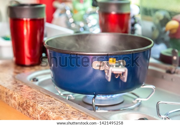 Water being boiled for dinner in a small teardrop\
camper kitchen with red\
mugs