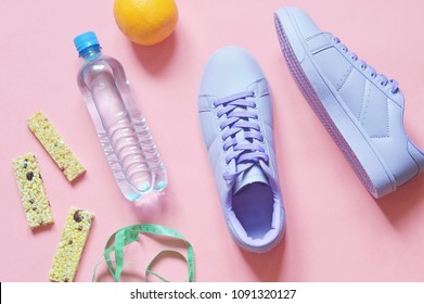 Water bottle, cereal energy bars, orange and purple sneakers on a pink background. Fitness food, workout, weight loss concept