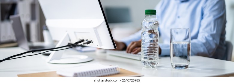 Water Bottle And Drinking Glass On Desk And Man Using Computer
