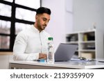 Water Bottle On Desk And Man In Foreground Using Computer