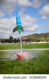 Water Bottle Rocket With Polka Dots Heavily Blurred From Being Launched At High Speed. Background Is A School Field Wand A Clidy Blue Sky