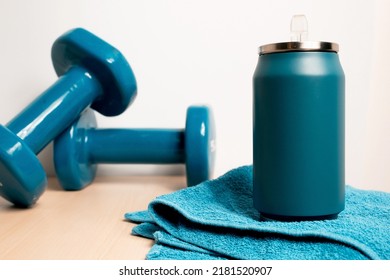 A Water Bottle Is Standing On A Towel. There Are Two Blue Dumbells In The Background