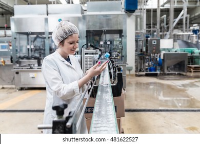 Water bottling line for processing and bottling pure mineral carbonated water into bottles. Female worker checking out water bottles. Selective focus on bottle.