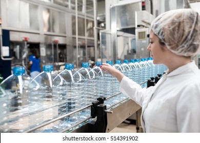Water bottling line for processing and bottling pure mineral water into bottles. Female worker checking out water bottles. Selective focus on woman's hand.