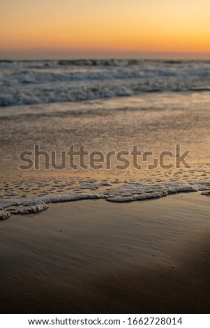 Water bubbles from an ebb and flow on wet sand during a sunset.