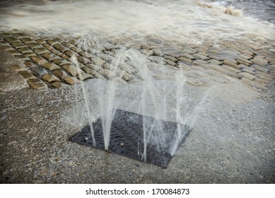 Water bursting from a drain into the road during severe floods.