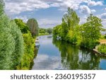 Water canal with green trees on bank of River Somme and small motor boats. Hortillonnages floating gardens jardins flottants waterways in marshy terrain in Amiens, Hauts-de-France Region, France