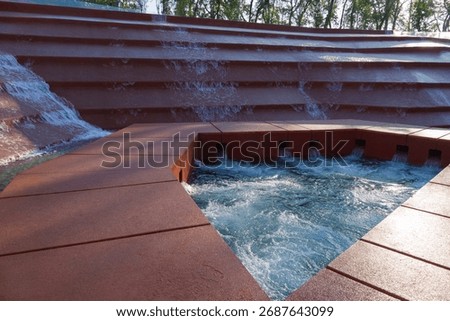 Water cascades down multi-tiered structure, forming abstract, geometric fountain surrounded by transparent glass railing. Amphitheater of water or Canyon in Public city park Krasnodar or Galitsky Park