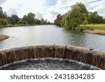water cascading over a weir in a lake with trees and countryside in the background