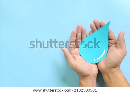 Water conservation and access to safe drinking water concept. Top view of human hands holding blue water drop with copy space.