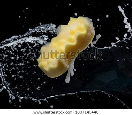 Water containing soap splashing with yellow sponge isolated on black background