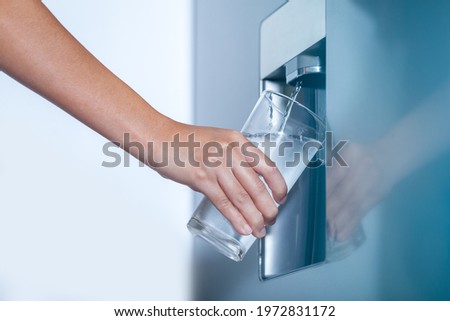 Water dispenser from dispenser of home fridge, Woman is filling a glass with water from the refrigerator.
