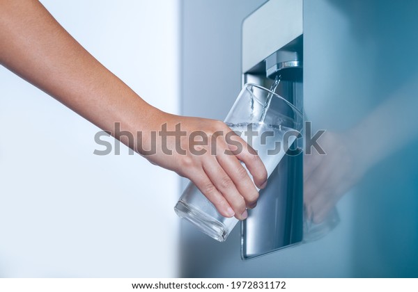 Water dispenser from\
dispenser of home fridge, Woman is filling a glass with water from\
the refrigerator.