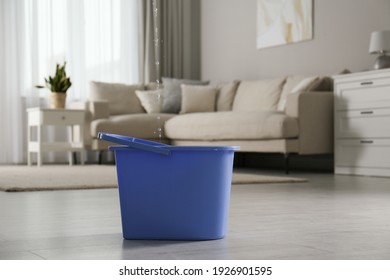 Water Dripping From Ceiling Into Plastic Bucket On Floor In Living Room. Leaking Roof