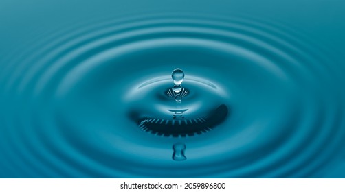 Water Drop  Falling On Water Surface Created Ripples With Nay Blue Background.