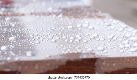 Water drop on reflective clear plastic wrap on wooden table - Powered by Shutterstock