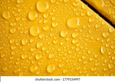 Water droplet on the car hood. Water beading after rain or car wash on yellow shiny paint surface. Beading created by ceramic coat or paint sealant with high surface tension. Water drop background.