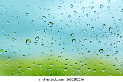 Water Droplets On A Car Glass On A Background Of Blue Sky And Green Grass. Water Drop Texture As A Background. Freshness After Rain. Wet Clean Nature, Ecology. Wet Window.