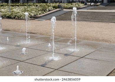 Water droplets spread from the fountain in the air. Splashing water from a fountain in the park. Vertical fountain jets in the sidewalk on the square in the city park. - Powered by Shutterstock